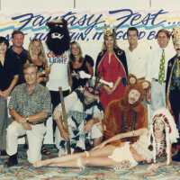 A group of unknown people standing in front of a Fantasy Fest sign.
