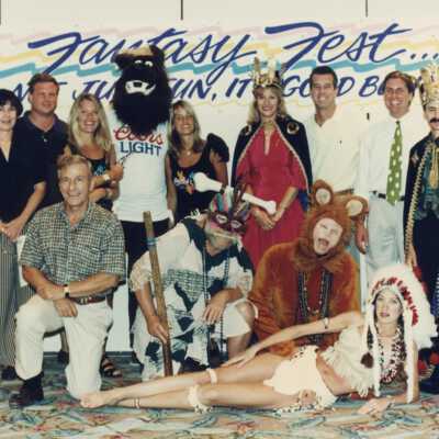 A group of unknown people standing in front of a Fantasy Fest sign.
