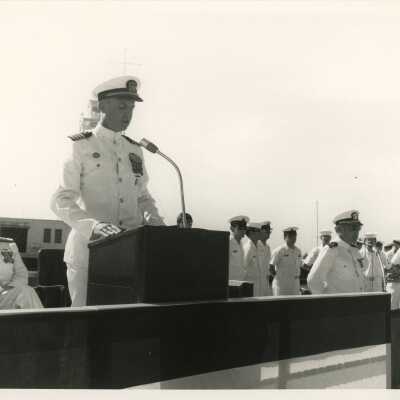 Men in uniform at a ceremony, one standing at the podium