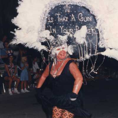 Unknown woman dressed up, her head piece reads is that a gun in your pocket.