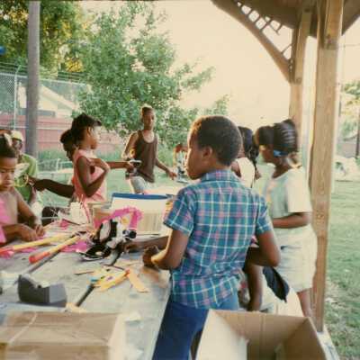 A group of unknown kids working on some crafts at a table outside.