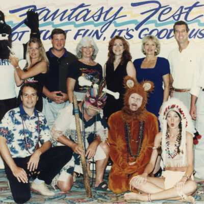 A group of unknown people standing in front of a Fantasy Fest sign.