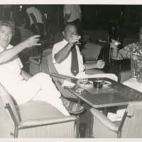 3 Unknown men sitting at a table holding drinks up