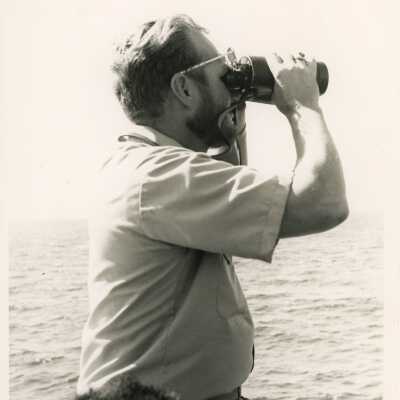 U.S. Navy man looking out into the ocean with binoculars