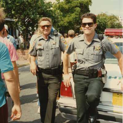 Two unknown cops leaning against the cop car.