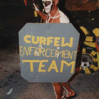 An unknown man dressed up holding a sign that reads curfew enforcement team.