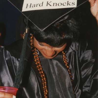 Unknown woman dressed up with a cap and gown that read University of Hard Knocks.