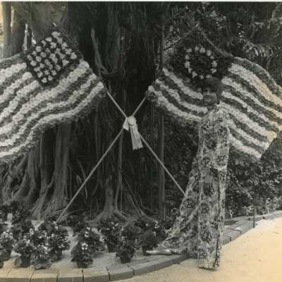 An unknown woman standing next to a tree and 2 flags