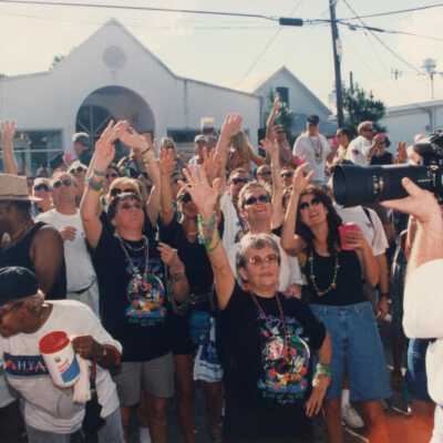 Unknown people in the street looking up and holding an arm up in the air.