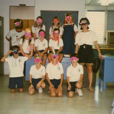 A group of unknown school kids with two unknown adults all wearing face mask.