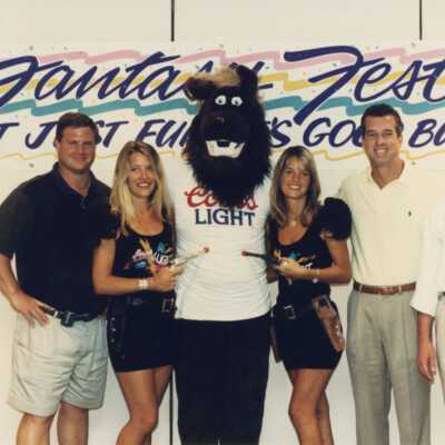 A group of unknown people standing in front of a Fantasy Fest sign.