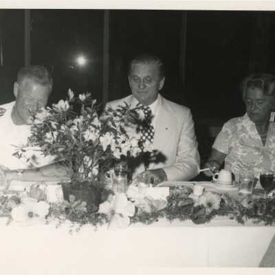 3 Unknown people sitting at a table at a party, one is in uniform