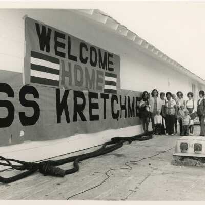 A group of unknown people standing next to a welcome home sign