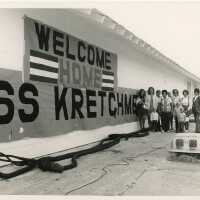A group of unknown people standing next to a welcome home sign