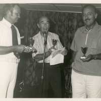 3 Unknown men standing at a microphone each holding a trophy