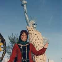 An unknown lady dressed up standing next to a float that has a statue of liberty on it.