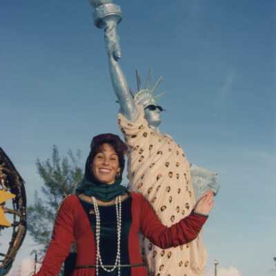 An unknown lady dressed up standing next to a float that has a statue of liberty on it.
