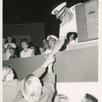 An unknown man at a podium leaning over and shaking hands