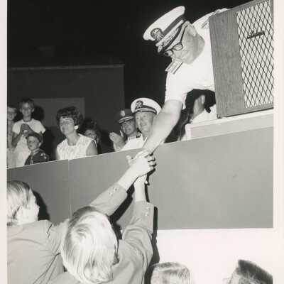 An unknown man at a podium leaning over and shaking hands