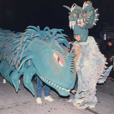 A dragon in the parade being moved down the street with unknown people under it.