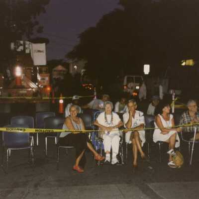 Unknown people sitting on chairs in a taped off area.