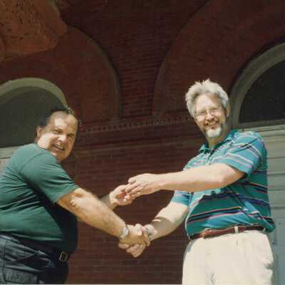 Two unknown men shaking hands standing outside.