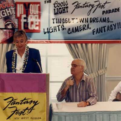 Unknown woman speaking at the podium at the Fantasy Fest meeting.