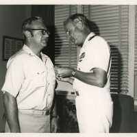 2 Unknown men in uniform, one is putting a pin on the others shirt