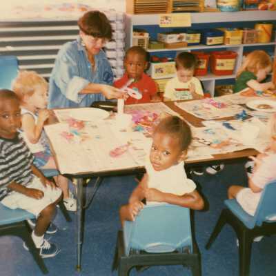 Unknown teacher and kids working in a classroom at a table.