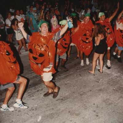 Unknown people dressed up as pumpkins walking in the street for the parade.