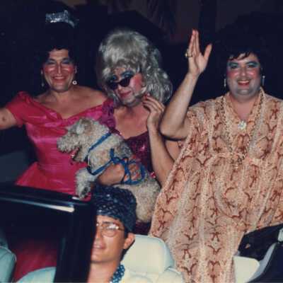 Unknown people dressed up, sitting on top of the back seat of a convertible.