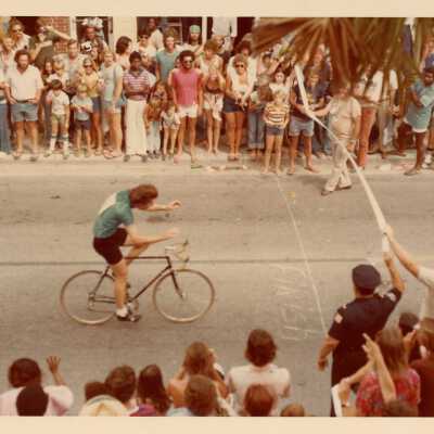 Unknown man riding a bike down a street with people watching