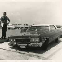 2 Unknown men in uniform standing on a pier next to an old car