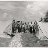 A group of unknown men and children standing next to tents