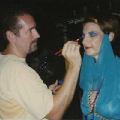 Unknown man putting make up on an unknown woman who is dressed up.