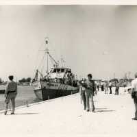 A group of unknown people on a pier with a few boats
