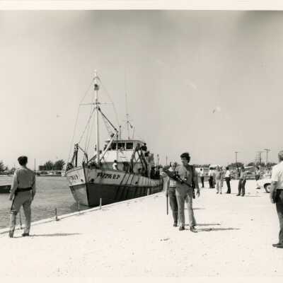 A group of unknown people on a pier with a few boats
