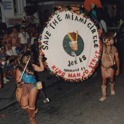 A group of unknown people in the parade holding a sign that reads Save the Miami circle.
