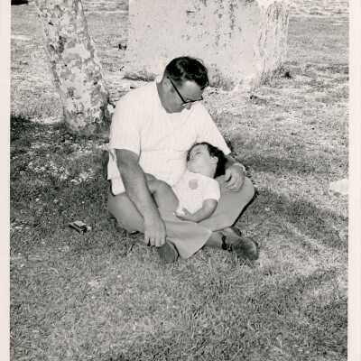 An unknown man holding a sleeping baby on the lawn