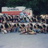 A group of unknown people in front of a car, they all have the same shirts on.