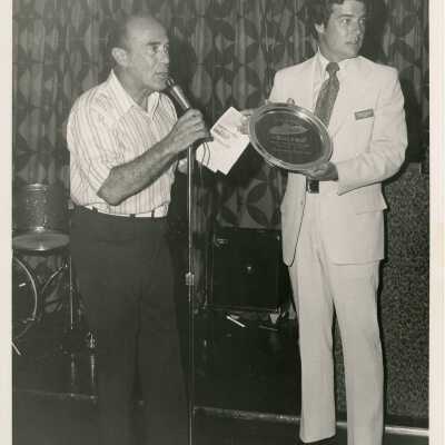 2 Unknown men standing at a microphone, one holding a plaque