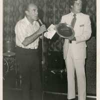 2 Unknown men standing at a microphone, one holding a plaque