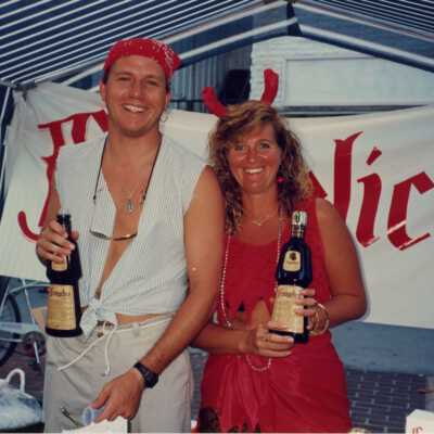 Two unknown people dressed up and holding bottles of alcohol at the street fair.