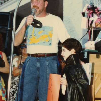 Unknown man talking into a microphone with a child dressed up standing next to him.