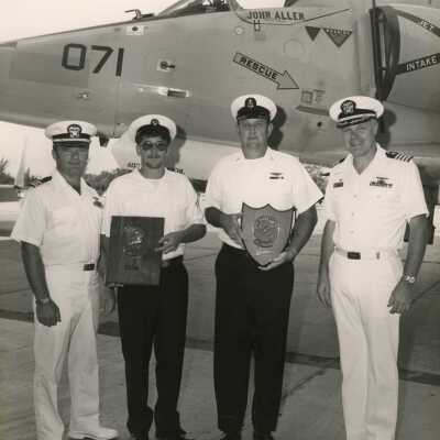 U.S. Navy men next to a jet holding plaques