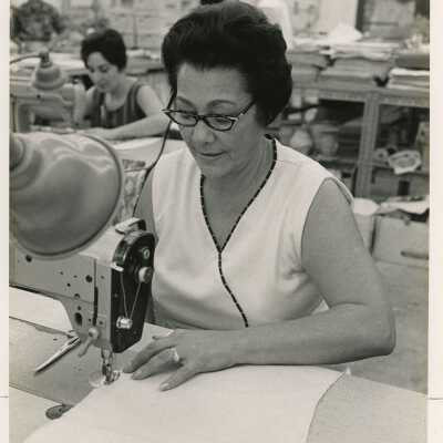An unknown woman sewing in a room with others doing the same