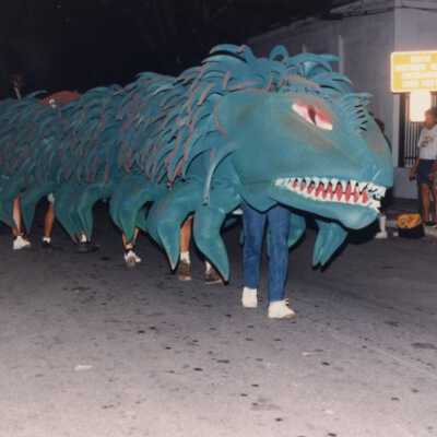 A dragon in the parade being moved down the street with unknown people under it.
