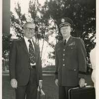 2 Unknown men standing outside, one is uniform