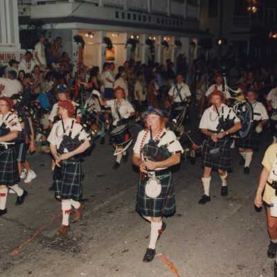 A pipe band playing while walking down the street in the parade.