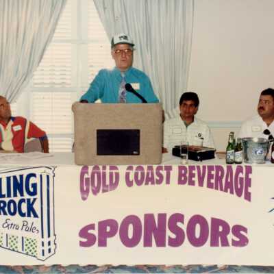 An unknown man speaking at the podium, a sign reads Gold Coast beverage sponsors under him.
